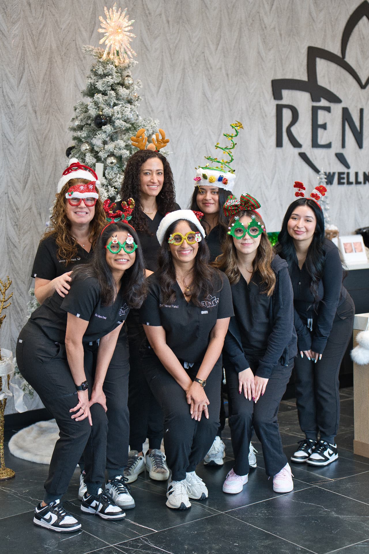 The Renew Wellness Center team in festive holiday glasses and hats in front of the Christmas tree